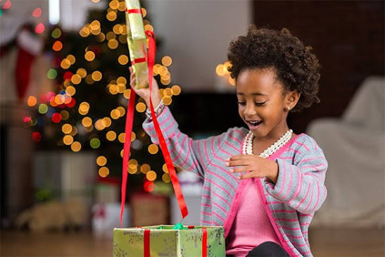 Niña abriendo un regalo junto a un árbol de Navidad